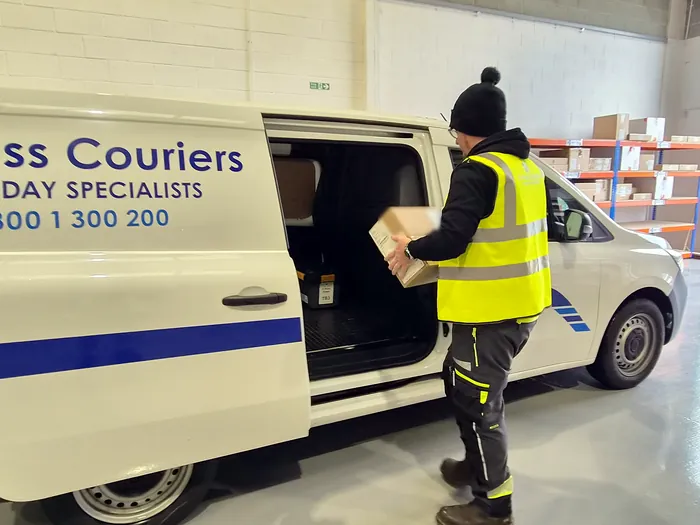 An X-Press Couriers team member in hi-vis loading a parcel into a liveried van